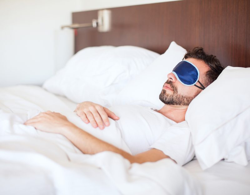 Portrait of a young man with a beard using a sleep mask to get some rest in a hotel