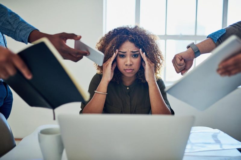 Woman in front of her computer at the office looking stressed and surrounded by arms requiring her to work