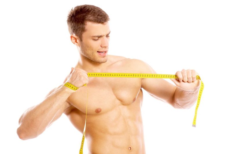 Fotografía de ginecomastia y culturismo mostrando a un hombre musculoso sin camiseta y bronceado con una cinta de medir